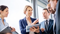 Mature businesswoman explaining new business ideas to colleagues during a standing meeting in office Mature businesswoman explaining new business ideas to colleagues during a standing meeting in office